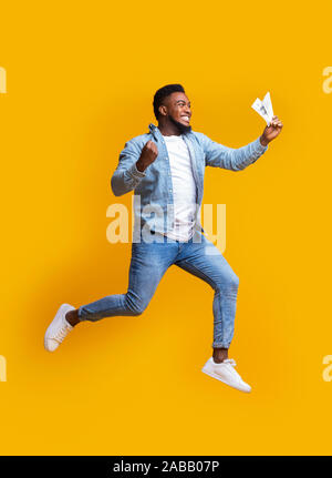 Euphorisch afro Mann springen mit Bargeld in der Hand auf gelbem Hintergrund Stockfoto