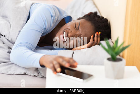 Afro Frau mit Migräne im Bett Weckdienst Ausschalten Stockfoto