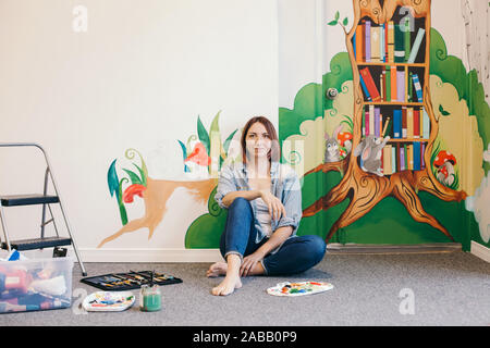 Kreatives Hobby und freie künstlerische Arbeit Nebenjob Konzept. Kaukasische Frau artist Entspannung nach Hand Malerei Wandbilder auf Wänden innen im Apartment o Stockfoto