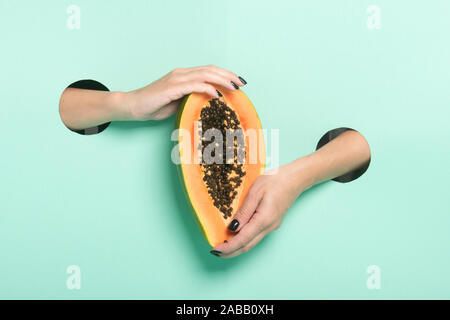 Weibliche Hände halten frischer Papaya durch ein Loch auf Neon mint Hintergrund. Stockfoto
