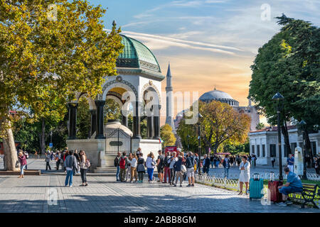 Touristen Pass von der Deutschen Brunnen, ein Pavillon gestaltete Brunnen in Sultanahmet Square mit der Hagia Sophia in der Ferne. Stockfoto