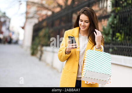 Lächelnde Frau in einem gelben über mobile und halten Sie die Taschen von Shopping Mantel Stockfoto