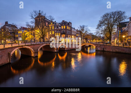 Nacht Blick auf Amsterdam Stadtbild mit Canal, die Brücke und die mittelalterlichen Häuser in der Dämmerung beleuchtet. Amsterdam, Niederlande Stockfoto