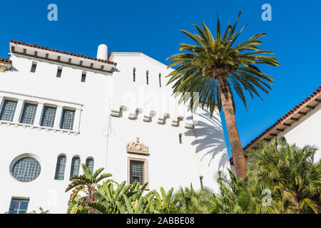 Eine Palme und ein historisches weißes Spanish Colonial Revival Architektur Stil Gebäude mit verzierten Fenstern und Verkleidung in Santa Barbara, Kalifornien, USA Stockfoto