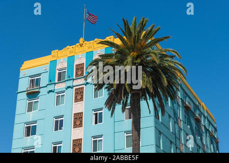 Angewinkelte Front- und Seitenansicht eines blauen Gebäude im Art-Deco-Stil mit gelber Rand mit einer amerikanischen Flagge auf dem Dach und eine Palme vor Stockfoto