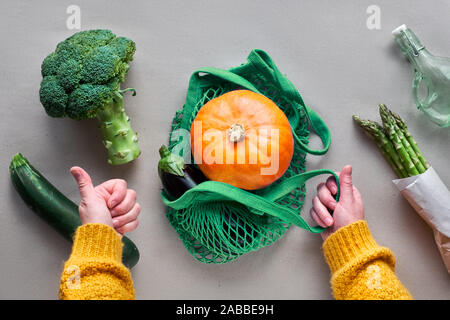 Umweltfreundliche null Abfall flach mit Händen halten String Tasche mit orange Kürbis. Flach in Grün und Orange mit Gemüse und Hände auf Handwerk Papier Stockfoto