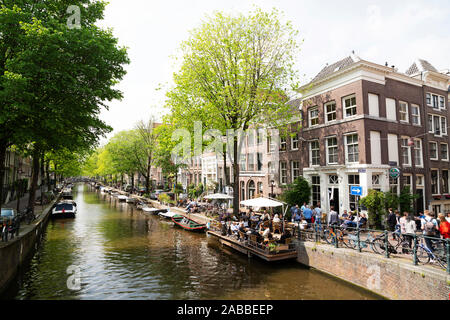 Frühling in Amsterdam, Niederlande. Die Leute sitzen in einem Café im Freien an einem Kanal. Stockfoto