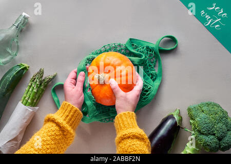 Umweltfreundliche null Abfall flach mit Händen hält String Tasche mit orange Kürbis. Flach in Orange und Grün mit Gemüse auf Handwerk Papier. Stockfoto