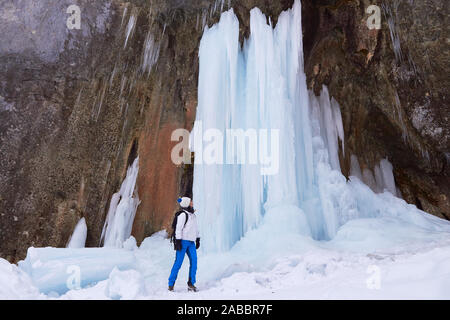 Frau Wanderer neben einem hohen gefrorenen Wasserfall bei einer Winterwanderung bei sieben Leitern Canyon (7 Scari) massiv in Piatra Mare, Brasov, Rumänien. Stockfoto