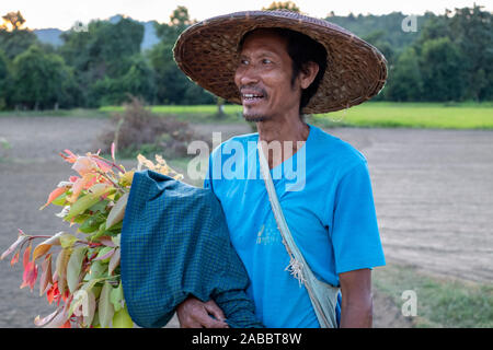 Burmesischen Bauern in konischer Asiatischen Reis Hut kehrt in das Dorf entlang der Chindwin Fluss im Nordwesten Myanmar (Birma) mit frisch geschnittenen Blumen Stockfoto