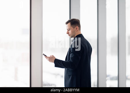 Business Mann mit Handy app im Flughafen. Young Business professionelle man texting Smartphone wandern im Bürogebäude oder Flughafen Terminal Stockfoto