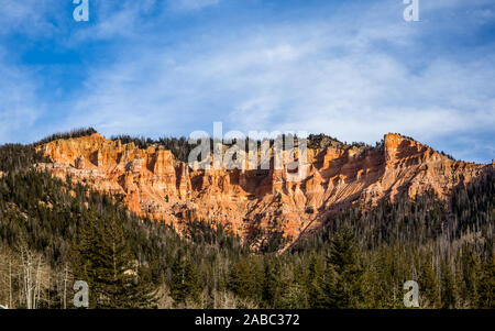 Roten Felstürme und Hoodoos des südlichen Utah Bryce Canyon oder Cedar Breaks über grüne Wälder im frühen Winter. Blauer Himmel mit Wolken whispy Overhead Stockfoto