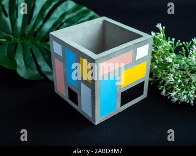 Cactus pot. Wunderschön bemalte konkrete Pot. Leer moderne Kubikmeter Beton Pflanzmaschine mit Blumen und palm leaf auf dunklem Hintergrund. Stockfoto