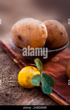 Nahaufnahme von organischen Kartoffel in einem Ton Schüssel auf jutesäcken und einige frische Zitronen auch. Vertikale erschossen. Stockfoto