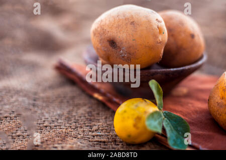 Nahaufnahme von organischen Kartoffel in einem Ton Schüssel auf jutesäcken und einige frische Zitronen auch. Horizontale erschossen. Stockfoto