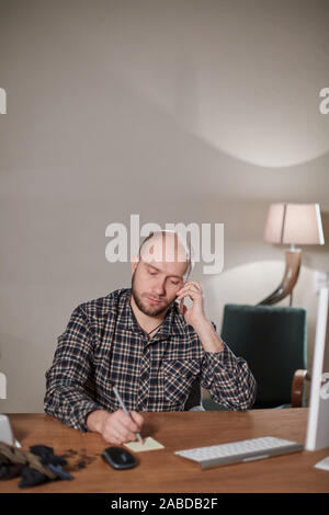 Ernster Mann sprechen per Telefon. Auf dem Computer ist die Lieferung der Online Store. Arbeiten mit der Nähmaschine in einer Textil- Studio. Schneider macht Stockfoto