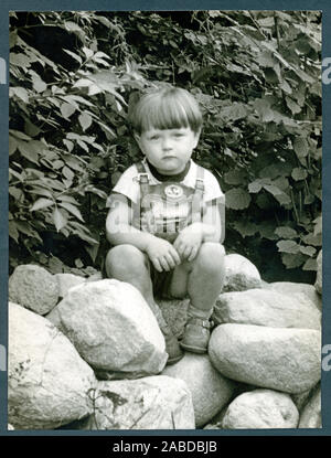 Europa, Deutschland, Hamburg, kleiner Junge in Lederhose mit Feldsteinen sitzt und schaut traurig in die Kamera, 1950er Jahre. /Europa, Deutschland, Hamburg, kleiner Junge aus Leder Hosen sitzen auf kleinen Steine ist, sieht er leider an den Fotografen, 1950. Stockfoto