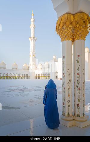 Frau, die während des Sonnenuntergangs die Abu Dhabi Moschee steht. Stockfoto