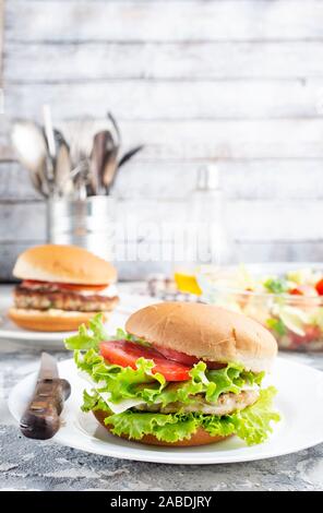 Chicken Burger in der Nähe auf einem weißen Teller. Burger, Käse, Salat, Schinken, Tomate und weißer Soße. Stockfoto