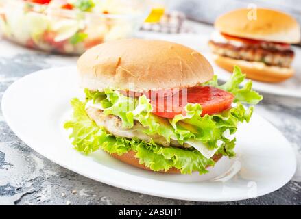 Chicken Burger in der Nähe auf einem weißen Teller. Burger, Käse, Salat, Schinken, Tomate und weißer Soße. Stockfoto