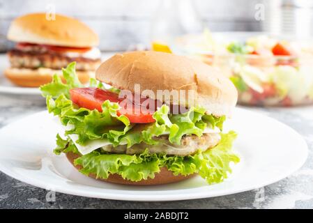 Chicken Burger in der Nähe auf einem weißen Teller. Burger, Käse, Salat, Schinken, Tomate und weißer Soße. Stockfoto