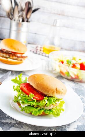 Chicken Burger in der Nähe auf einem weißen Teller. Burger, Käse, Salat, Schinken, Tomate und weißer Soße. Stockfoto