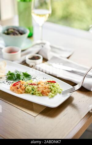 Nahaufnahme von gesalzenem und geräuchertem Lachs oder Forelle auf einer Gabel. Lachstatar mit Gurke und Sesam. Verkostung Teller auf einen hölzernen Tisch. Stockfoto