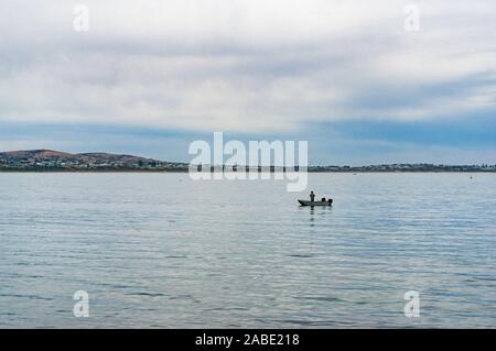 Mann in die Fischerboot auf ruhiger See mit weit entfernten Ufer anzeigen Stockfoto