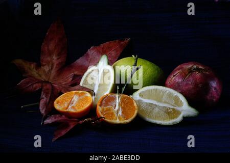 Zitrone und Mandarine mit offenem Gesicht auf Ahorn Blätter gegen einen schwarzen und blauen Hintergrund Stockfoto