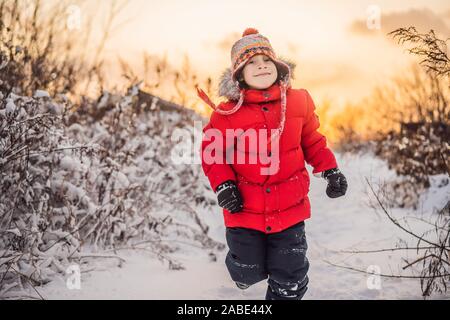 Cute boy in red Winterkleidung läuft Spaß im Schnee. Winter Spaß im Freien Konzepte Stockfoto