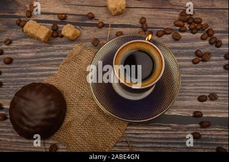 Eine Tasse Kaffee, Marshmallows in Schokolade, Kaffee Bohnen, brauner Zucker auf einer hölzernen Hintergrund. Nahaufnahme Stockfoto