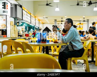 Singapur - 17 Mär 2019 - einen mittleren Alters asiatische Chinesische Singaporean Mann in der Bürokleidung genießt eine bis spät in die Nacht Bier in einem Lokal/Coffeeshop/das kopitiam, Stockfoto