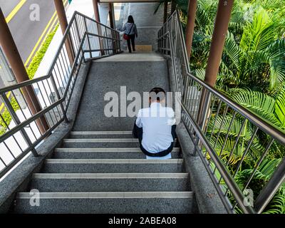 Singapur - 3. Mai 2019 - Eine erschöpfte Asiatische chinesische Mann sitzt und nimmt einen Rest/nap im Schatten auf einer überdachten Brücke während seiner Pause. Stockfoto