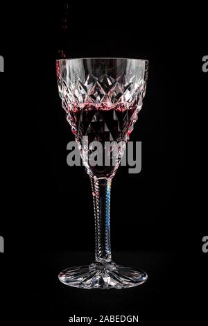 Rotwein in einem geschliffenen Kristall Glas Wein auf einem schwarzen Hintergrund isoliert Stockfoto