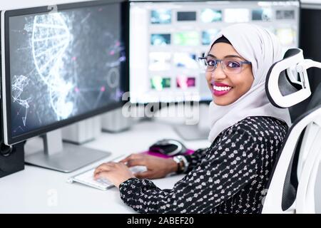 Junge afro-amerikanische moderne muslimische business Frau mit Kopftuch mit Kreativen hellen Büro Arbeitsplatz mit großen Bildschirm Stockfoto