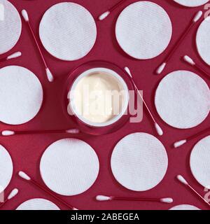 Hygiene Produkte: Weiße runde Wattepads und Kunststoff Sticks für die Reinigung der Ohren liegen auf einem rosa Hintergrund nächste Creme zu Gesicht Stockfoto