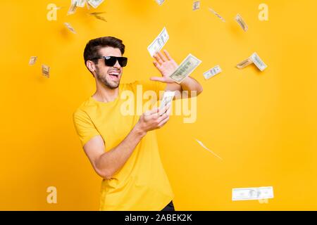 Foto der jungen Hübschen unvorsichtigen Kerl Geld Banknoten entfernt wohlhabende Person tragen Sun specs casual t-shirt isolierte helle gelbe Farbe Stockfoto