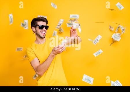 Foto der jungen Hübschen unvorsichtigen Kerl werfen usa Geld Banknoten entfernt wohlhabende Person tragen Sun specs casual t-shirt helle gelbe Farbe isoliert Stockfoto