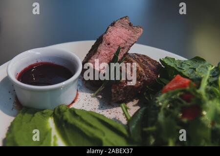 Saftige medium Steak auf dem weißen Teller im Restaurant. Fleisch serviert mit Salat Kartoffelpüree Spinat und Preiselbeersoße. Stockfoto