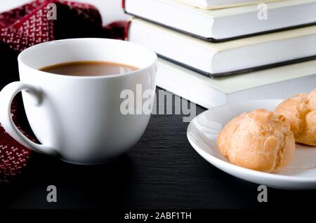 Eine runde weiße Tasse und Untertasse steht auf einem weißen Tisch neben Büchern und gelben Blätter im Herbst Stockfoto