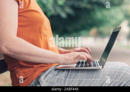 Frau mit Laptop auf der Straße Bank,. Nach kaukasischen weibliche Blogger ist die Eingabe über Tastatur, arbeiten überall vom Home Office Stockfoto