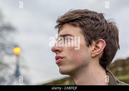 Ein junger Mann in seinen späten Teens oder Anfang der 20er Jahre steht im Freien mit einem ernsten Ausdruck, als er in die Ferne schaut. Stockfoto