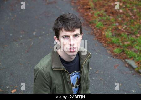 Einen attraktiven jungen Mann in seinen späten Teens oder Anfang der 20er Jahre steht in einem Park bis in die Kamera schaut. Stockfoto