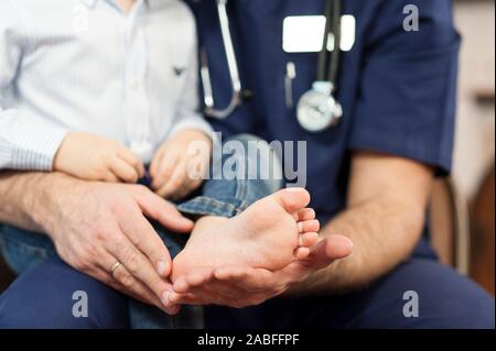 Der Kinderarzt untersucht die Füße des Kindes, der hautarzt behandelt die Fersen, Fuß und Ferse Massage. Konzept der Untersuchung und Behandlung von Kindern Stockfoto