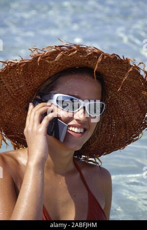 Portraet einer jungen Frau mit Sonnenhut, Sonnenbrille und handlich Stockfoto