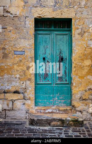 Grün lackierten Tor Eingang zu einem typischen Kalkstein Blockgebäude, St George, in Victoria, Gozo, Malta. Gelbe stuck Erodieren von Mauerwerk. Stockfoto