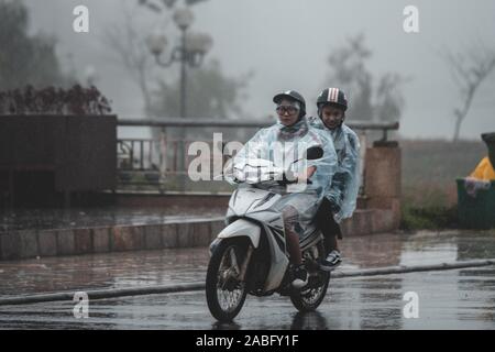 Zwei asiatische Männer reiten einen Roller im Regen - Sapa, Nordvietnam, Asien Stockfoto
