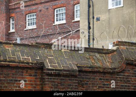 Groß und hohen Mauer mit Stacheldraht / Stacheldraht auf der Oberseite, für Zwecke der Sicherheit. Portsmouth Naval Base/Werft. UK. (105) Stockfoto