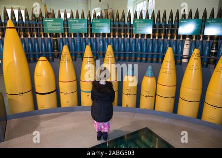 Kind, Mädchen im Alter von 4 Jahren an der Ausstellung von explosiven Granaten, die für die Verwendung durch militärische Kriegsschiffe in ihre Gewehre auf Marineschiffen. Explosion Museum der Naval Feuerkraft; ehemaliger Rüstung Depot der Royal Navy von priddy ist hart, in Gosport. Großbritannien (105) Stockfoto