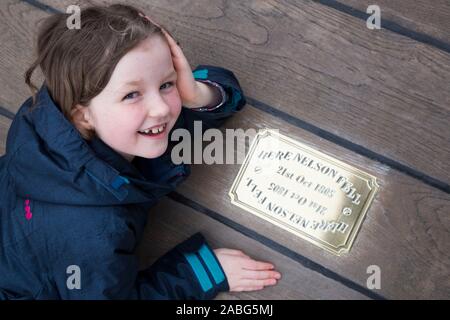 Kind Gast/kid Touristische untersuchen die Metall Messingschild auf der Website von HMS Victory an der Stelle, wo Admiral Lord Nelson fiel nach geschossen wird von einem französischen Musketier. Portsmouth. Großbritannien (105) Stockfoto